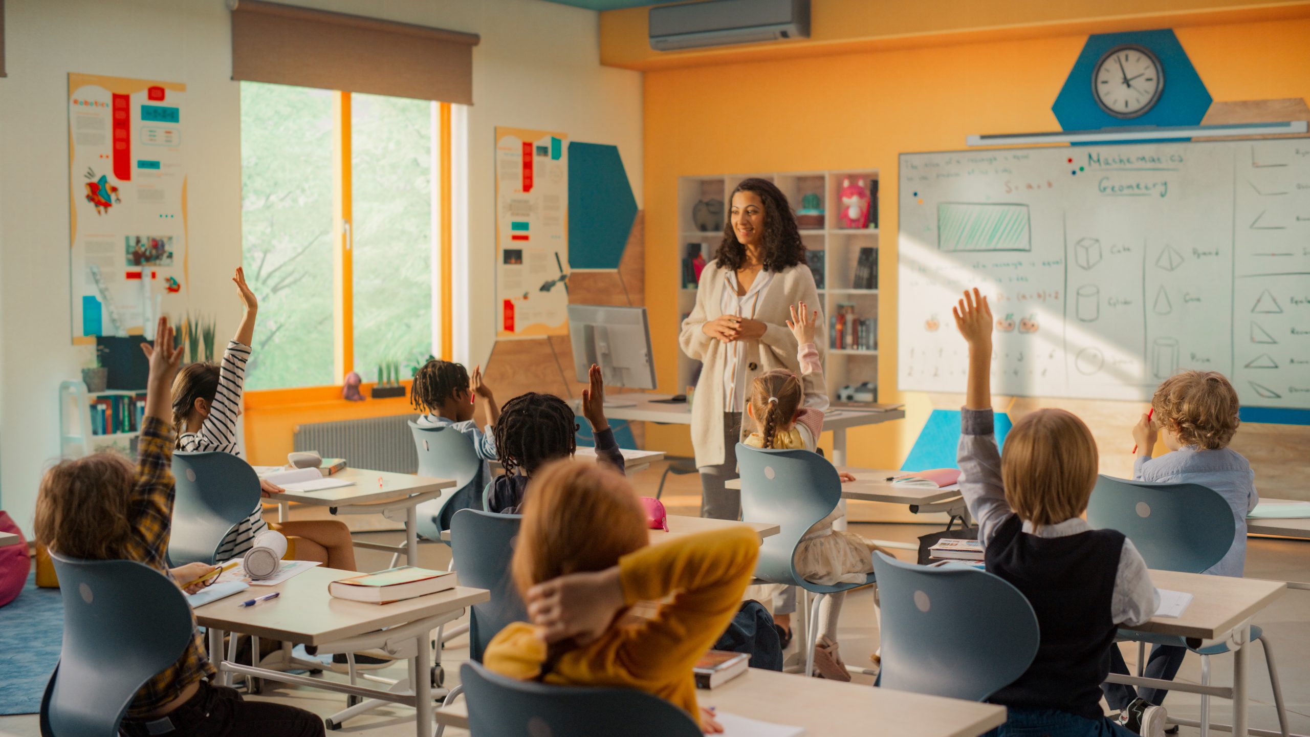 Elementary teacher leading whole-class instruction with diverse students actively raising hands to participate